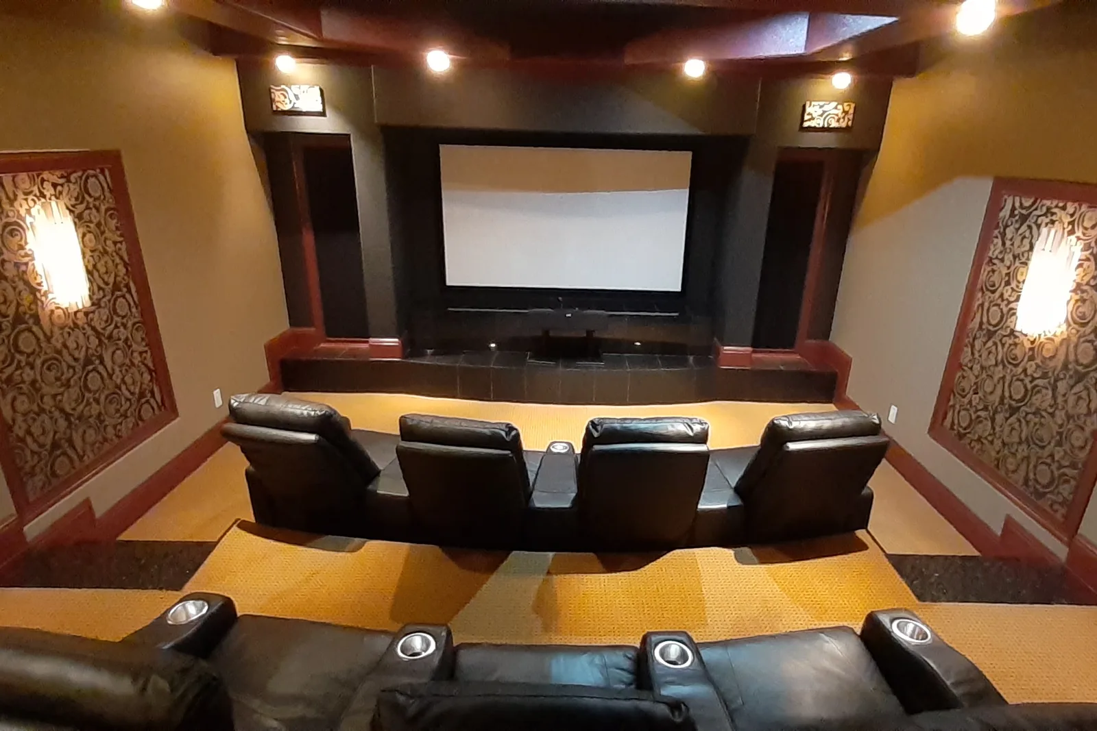 Stepped cinema room with red and gold damask acoustic panels, mahogany trim and black recliners