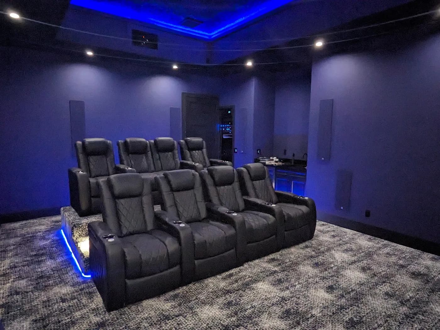 Media room lit by blue LED cove lighting above acoustic wall panels and tiered seating