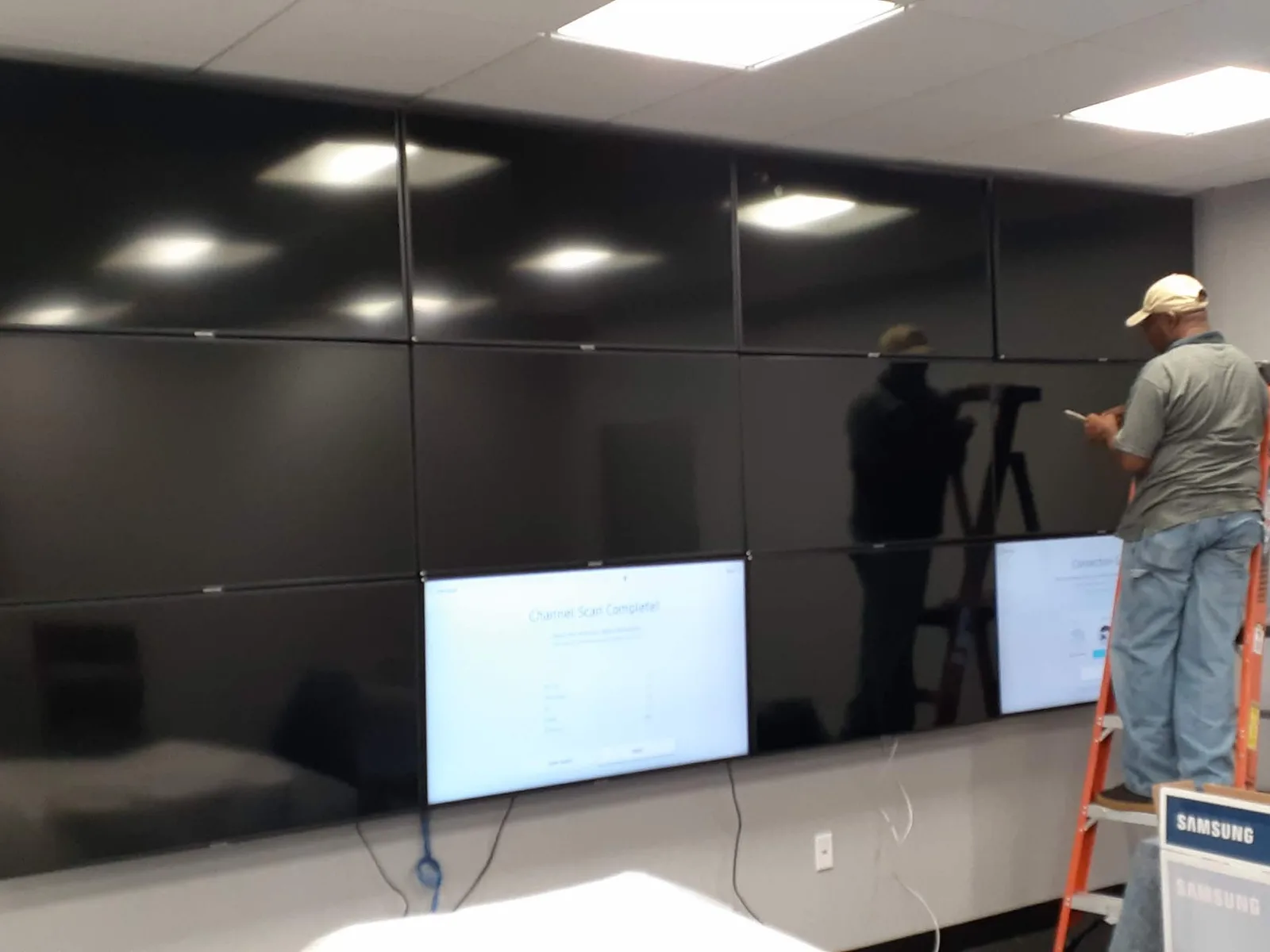 A technician on a ladder commissioning a twelve-panel video wall in an office