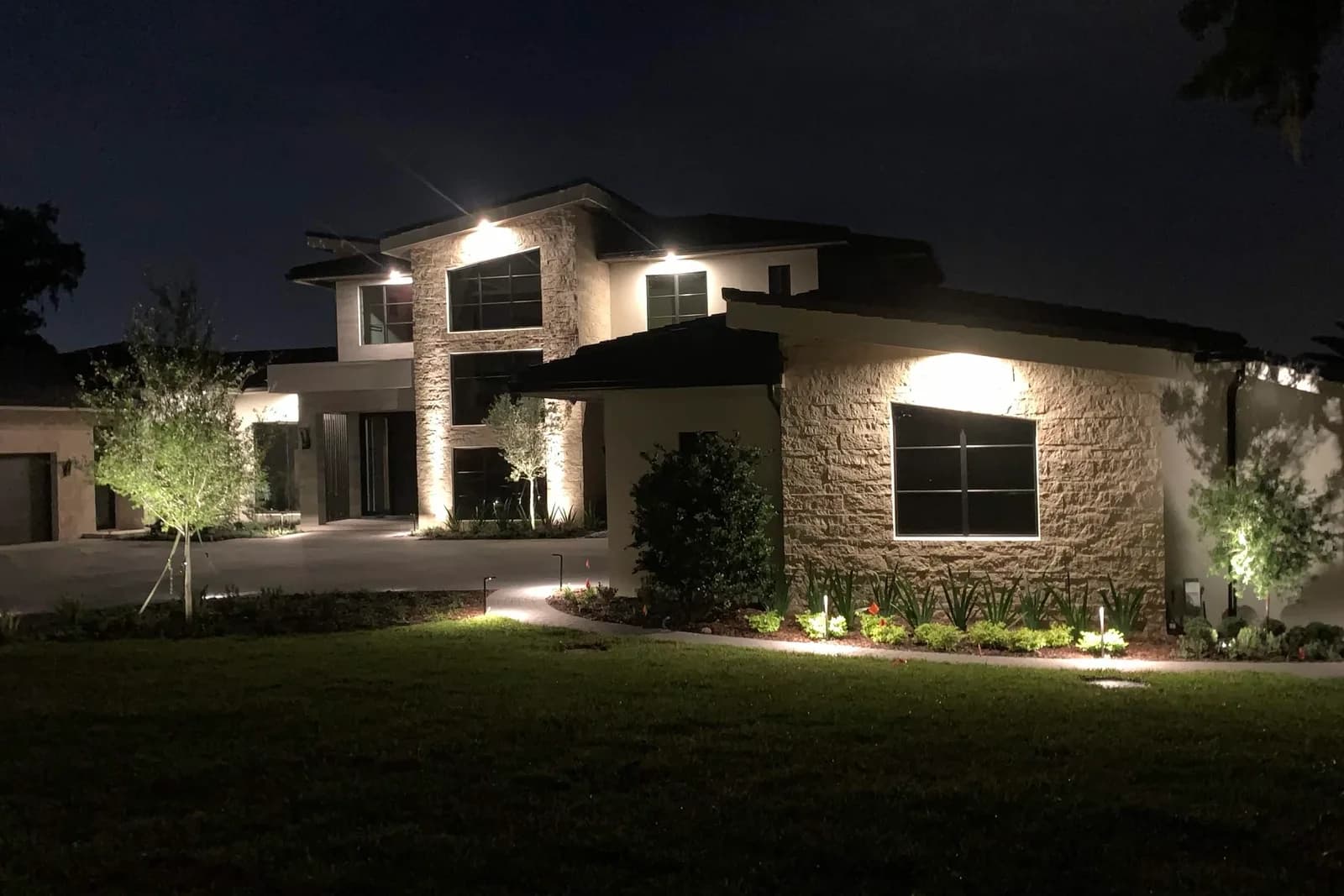 Modern two-story home at night with architectural and landscape lighting